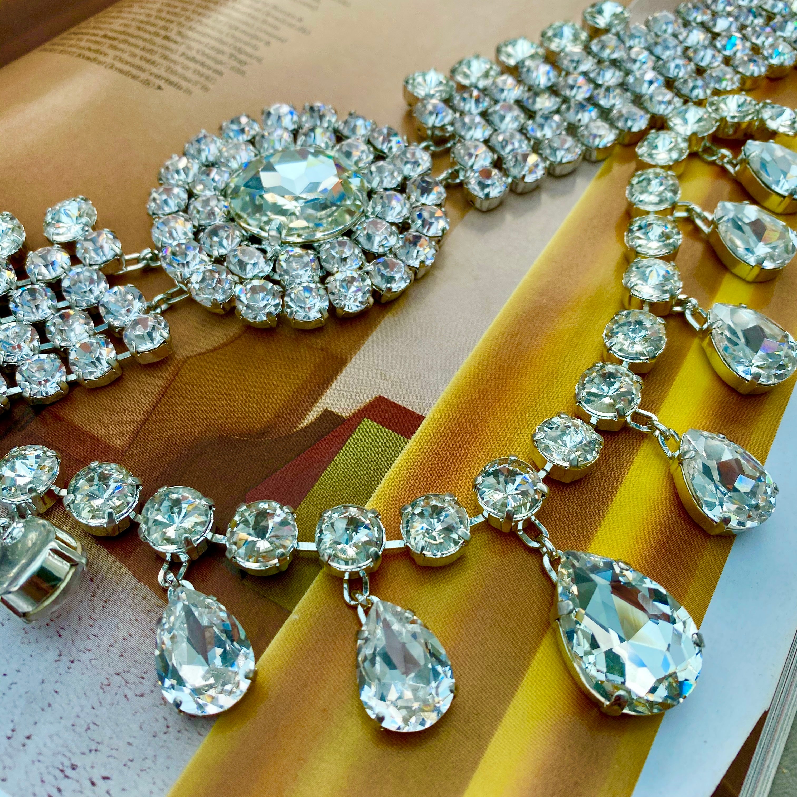 A close-up of a vintage-style choker necklace featuring a teardrop cascade design, encrusted with sparkling crystals.