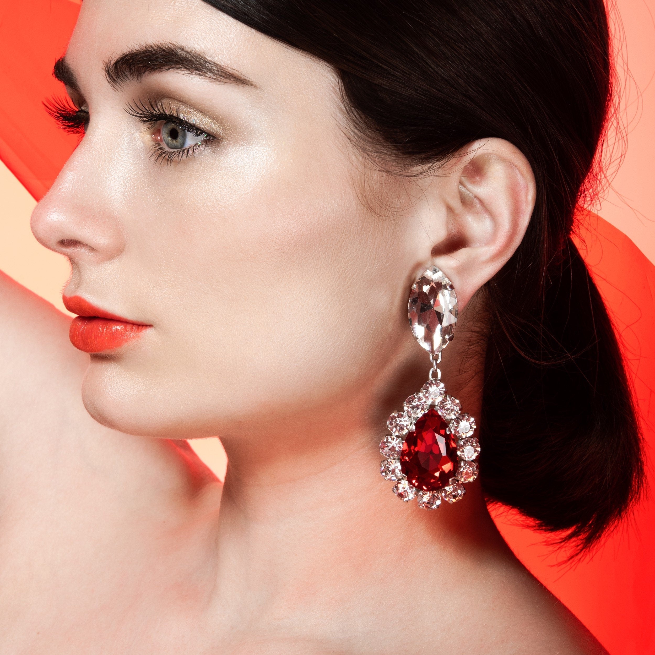 side shot of a ladies face wearing large earrings with red teardrop